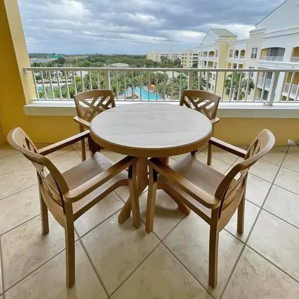 Outdoor balcony dining set with four Sanibel armchairs and a round Aquaba dining table overlooking a luxury resort pool and courtyard.